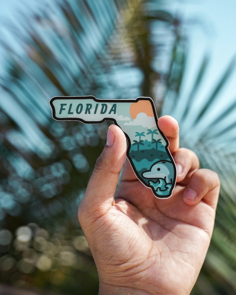 Hand holding Florida map sticker with palm trees.