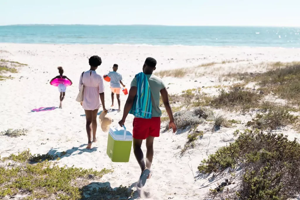 Family walking to beach carrying cooler and toys.